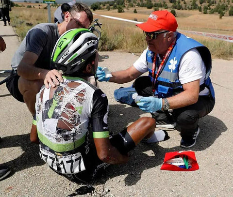 Cyclist receiving first aid on the roadside with first aid kit and emergency responders, illustrating use of first aid pouches for travel emergencies.