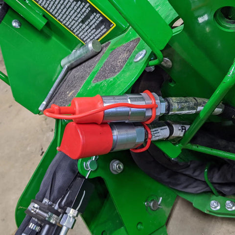 Dust caps for 1/2 inch flat-face hydraulic quick-connect couplers, red rubber with lanyards on a green skid-steer.