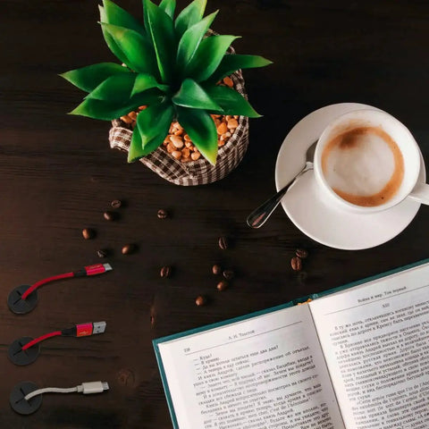 Top view of desk setup with coffee, plant, book, and 6 Pack 1 Inch Silicone Cable Grommets for Desk and TV Console Black with cables.