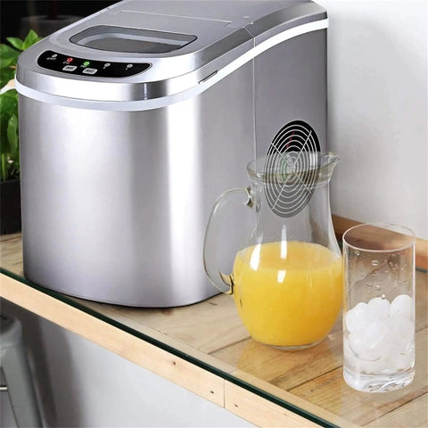 Front view of a stainless steel countertop ice maker with a digital control panel; juice pitcher and glass of ice nearby.