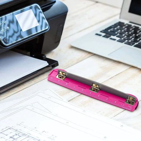 3 Hole Punch For Ring Binders With Built In Ruler on wooden desk near laptop and printer, deep pink ABS plastic, stainless steel punch heads