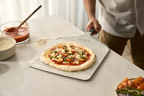 Compact 12 Inch Aluminum Pizza Peel With Handy Handle For Easy Pizza Turning And Oven Prep Lightweight Yet Durable Ideal For Home Kitchens And Ooni Ovens Space Saving Design For Quick Pies in use with raw pizza dough on countertop