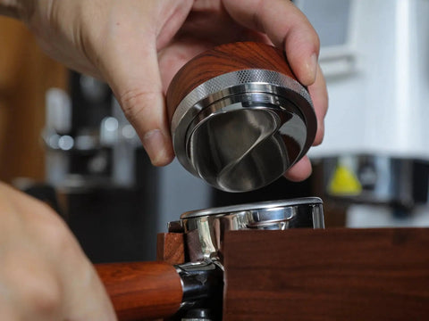 Close-up of a rosewood-handled KNODOS 54mm espresso distribution tool (stainless steel) being placed on a portafilter.