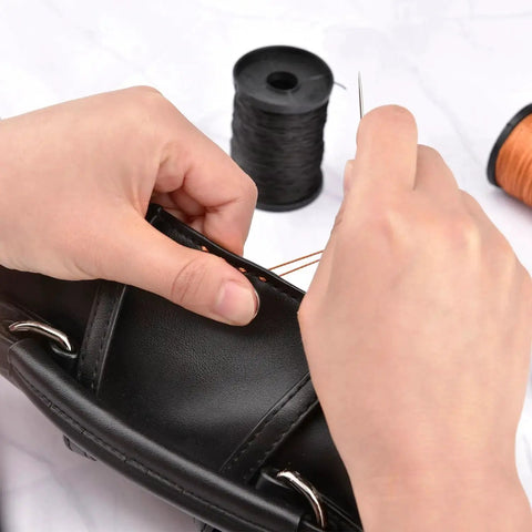 Person sewing leather with needle from Extra Strong Upholstery Repair Sewing Thread Kit With Heavy Duty Hand Needles Including Seven Styles Leather Canvas Sewing Needles And Three Rolls Nylon Thread 70 Yards Each In Three Colors For Carpets Upholstery Coats Tents Mattresses Furs And Leather.