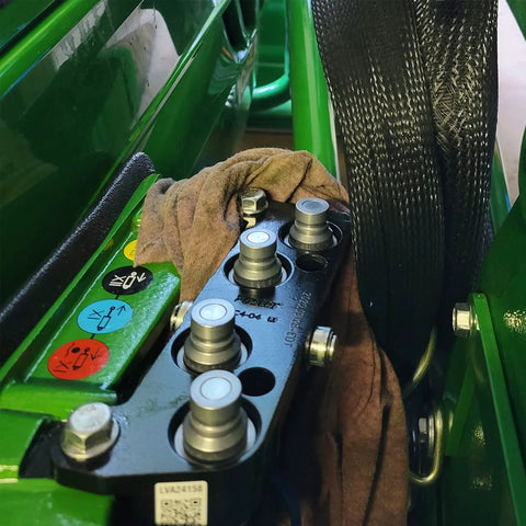 Five 3/4-in SAE hydraulic quick-connect couplers with dust caps on a mounting block beside green skid-steer equipment