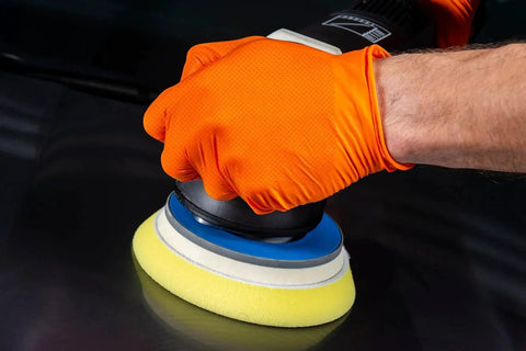 Hand wearing 8 Mil Orange Nitrile Gloves Heavy Duty Diamond Textured Industrial Food Handling, using a polisher on metal surface