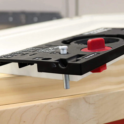 Close-up of concealed cabinet hinge jig with 35mm Forstner bit and metal bushing drill guide for precise hinge cup holes.