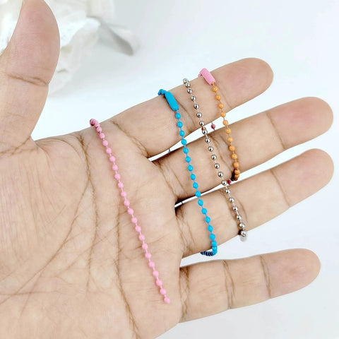 Hand holding assorted colored metal ball bead chains for DIY crafts, similar to 50 Pcs 4 Inch Ball Beads Chain With Connectors.