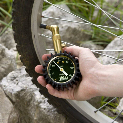 Hand-held JACO tire pressure gauge with brass nozzle attached to bicycle tire valve; black dial showing psi up to 60.