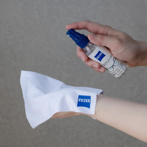 Person holding ZEISS Lens Cleaner 2oz Spray With Microfiber Cloth for coated lenses and optics, showcasing cleaning application.