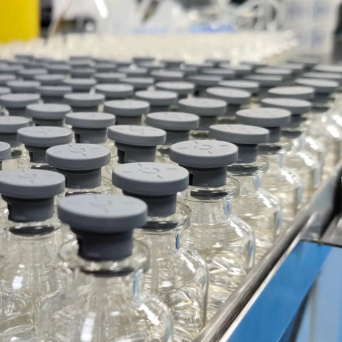 Glass vials with grey rubber stoppers on a production line