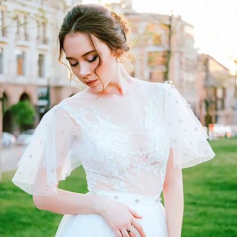 Woman in white lace dress with pearl embellishments standing outdoors, side view in urban setting
