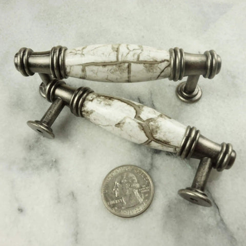 Antique-style cabinet pulls with marble handles next to a coin for size comparison on a gray surface.
