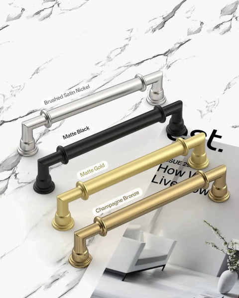 4 kitchen cabinet handles in brushed satin nickel, matte black, matte gold, and champagne bronze finishes on a marble surface.