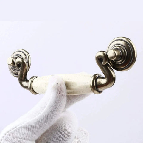 Close-up of a Set Of 4 4.5 Inch Ceramic Drop Handle Drawer Pulls In Antique Bronze Finish, held by gloved hand, showing ivory cream ceramic detail.