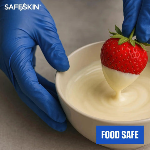 Person wearing Ultralight Nitrile Gloves 2.0 Mil Blue Large 100 Count Powder Free Latex Free, dipping strawberry in white chocolate.