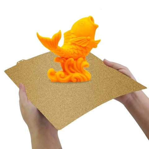 Hands holding Dual Sided Textured PEI Printing Bed For 3D Printers 235x235mm With Frosted PEI Surface with an orange 3D print.