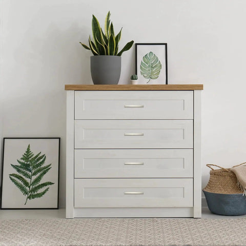 White dresser with four drawers and brushed nickel cabinet pulls, decorated with plants and wall art, modern bedroom decor