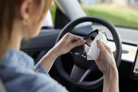 Person using ZEISS Pre-Moistened Sunglasses Cleaning Wipes For Smudge Removal 240 Count on sunglasses in a car.