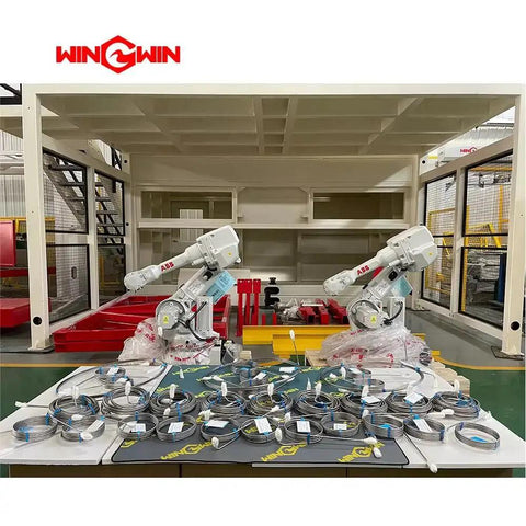 Two industrial robotic arms in a warehouse setting with coiled cables on a table