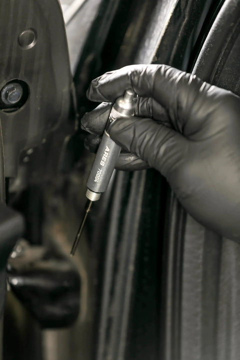 Precision Oiler Pen Applicator For Tight Spaces applying lubricant to a car door hinge, showing aluminum body and needle tip.