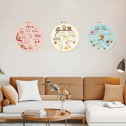 Three embroidery hoops with colorful pre-printed patterns on a living room wall. Beginner Embroidery And Cross Stitch Kit For Adults 3 Pack