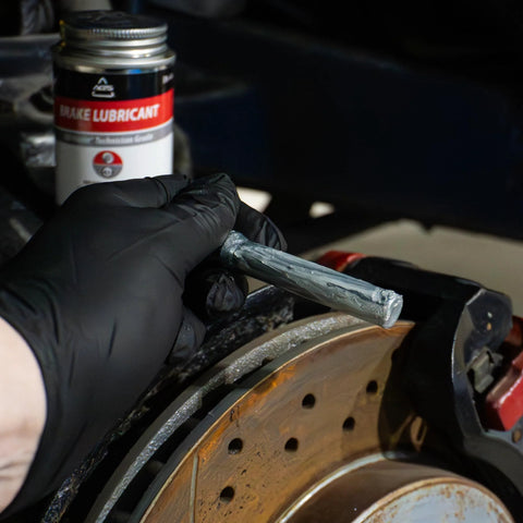 AGS 4oz Brush Top SIL-Glyde silicone brake grease applied to brake rotor by gloved hand; brake lubricant bottle visible