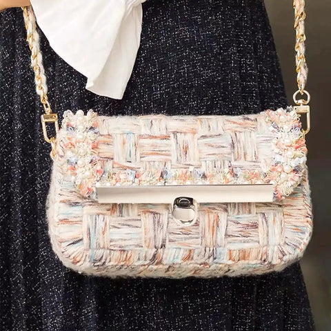 Woven handbag with multicolor pattern and gold chain strap, featuring a twist lock clasp. Fashion accessory for bags.