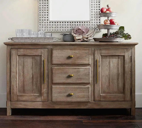 Wooden sideboard with antique brass finger pulls, three drawers and two cabinet doors, styled with decor and glassware.