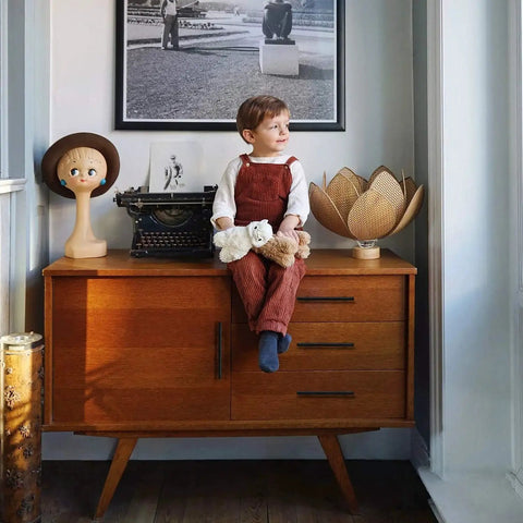 Child sitting on a mid-century modern cabinet with toys and decor items, including a vintage typewriter and a lamp with a lotus shade.