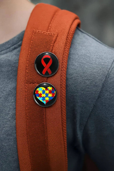 Two awareness pins on a red backpack, one with a red ribbon and the other with a heart made of colored puzzle pieces.