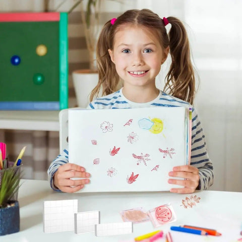 Child holding artwork with Six Clear Acrylic Stamp Blocks Set With Grid Lines For Easy Stamping Crafting And Scrapbooking visible on table.