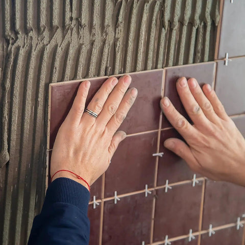 Hands installing tiles using One Sixteenth Inch Tile Spacers Set, 500 Pcs Cross Tile Leveling Clips for ceramic tile installation.