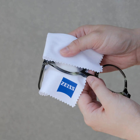 Person using ZEISS Lens Cleaner 2oz Spray With Microfiber Cloth For Coated Lenses And Optics on eyeglasses