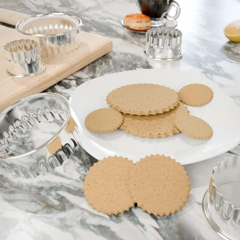 Fluted Round Cookie Cutter Set With Scalloped Biscuit And Circle Crinkle Cutters In Five Sizes Two Inch Through Three And A Half Inch Heavy Duty Food Grade Stainless Steel Rust Resistant With Comfortable Rolled Rim For Easy Handling on marble surface with cookies.