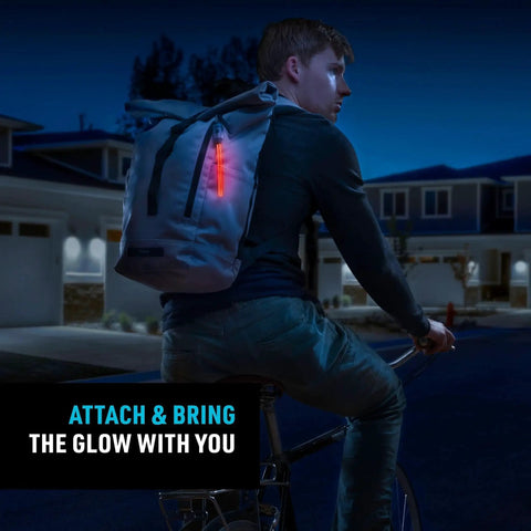 Nite Ize Radiant rechargeable LED glow stick with red glow attached to a gray backpack on a cyclist at night
