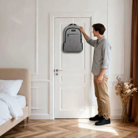 Person hanging a gray backpack on a white door in a modern bedroom with wooden floor and a beige bed.