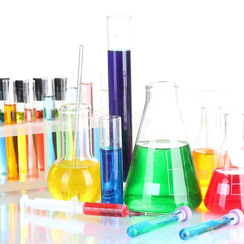 Assorted glass beakers and test tubes filled with colorful liquids, including green, blue, and yellow, displayed on a white background.