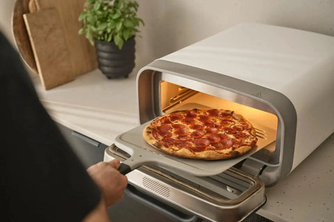 Compact 12 Inch Aluminum Pizza Peel With Handy Handle For Easy Pizza Turning And Oven Prep Lightweight Yet Durable Ideal For Home Kitchens And Ooni Ovens Space Saving Design For Quick Pies in use with pizza oven.