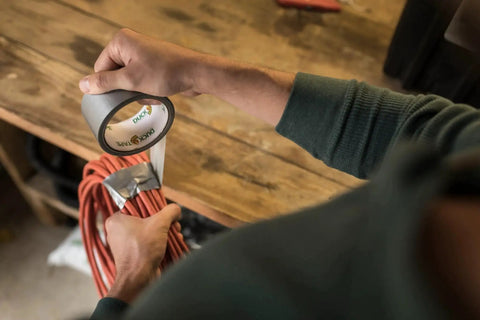 Person using Duct Tape 1.88 Inch By 60 Yard Silver For Quick Repairs And Sealing to secure red cables on a wooden workbench.