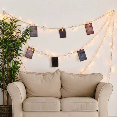 Cozy living room setup with string lights and photos hanging on wires above a beige loveseat and a green houseplant.