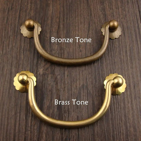 Six Pack Traditional Bail Cabinet Pulls In Antique Brass For Dresser Drawers And Cabinets, top view, bronze and brass tones, wood background.