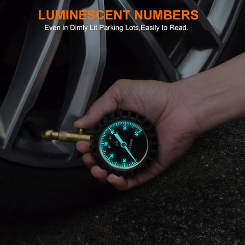 Tire pressure gauge, 2-inch glowing turquoise dial, hand-held near a car tire valve.