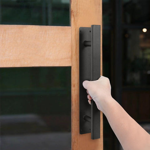 Hand holding Heavy Duty 12 Inch Metal Gate Pull Handles Pack Of 2 In Matte Black Iron Finish mounted on a wooden door
