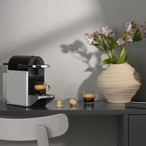 Pixie Aluminum Espresso Machine For Capsule Coffee Lovers on a countertop, brewing espresso, beside a vase of flowers.