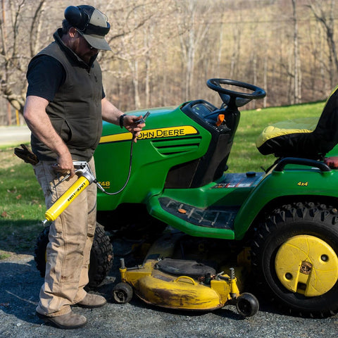 LockNLube Premium pistol-grip grease gun with 20-in hose and coupler, used to grease a green John Deere riding mower.