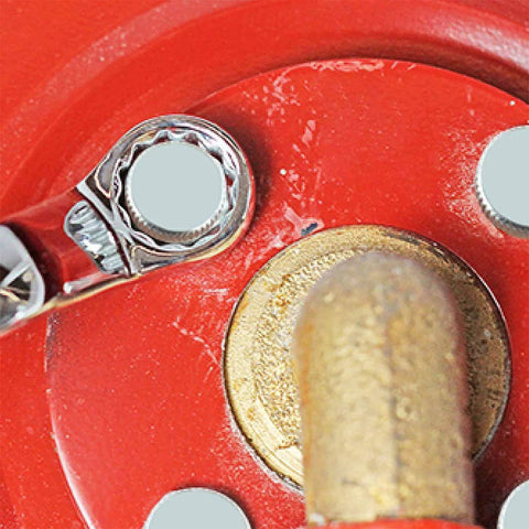 Close-up of a wrench tightening a bolt on a red metal surface with a brass fitting nearby