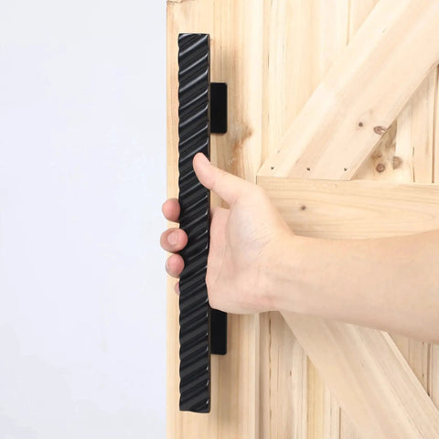 Hand holding solid brass sliding barn door handles set featuring 12 inch two sided design heavy duty mounting hardware installed