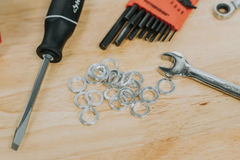Assorted tools on a wooden surface, including washers, a screwdriver, a wrench, and a hex key set.