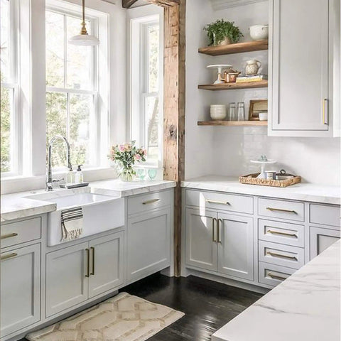Modern kitchen with white cabinets, glass windows, and wooden shelves, featuring a farmhouse sink and decorative accents.